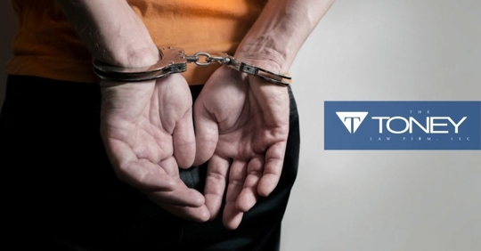 man in orange shirt with hands handcuffed behind his back