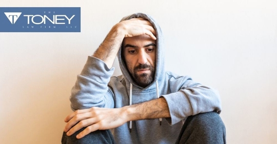 man in a sweatshirt with his hood up, hand on forehead, looking down and stressed