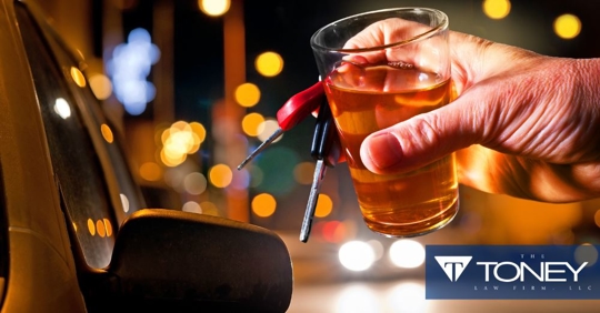 man's hand holding a glass of alcohol and car keys next to a car