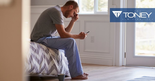 man upset looking at phone while sitting on edge of bed