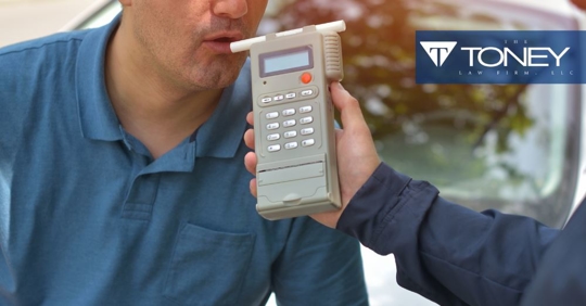 man blowing into a breathalyzer device while police officer holds the machine